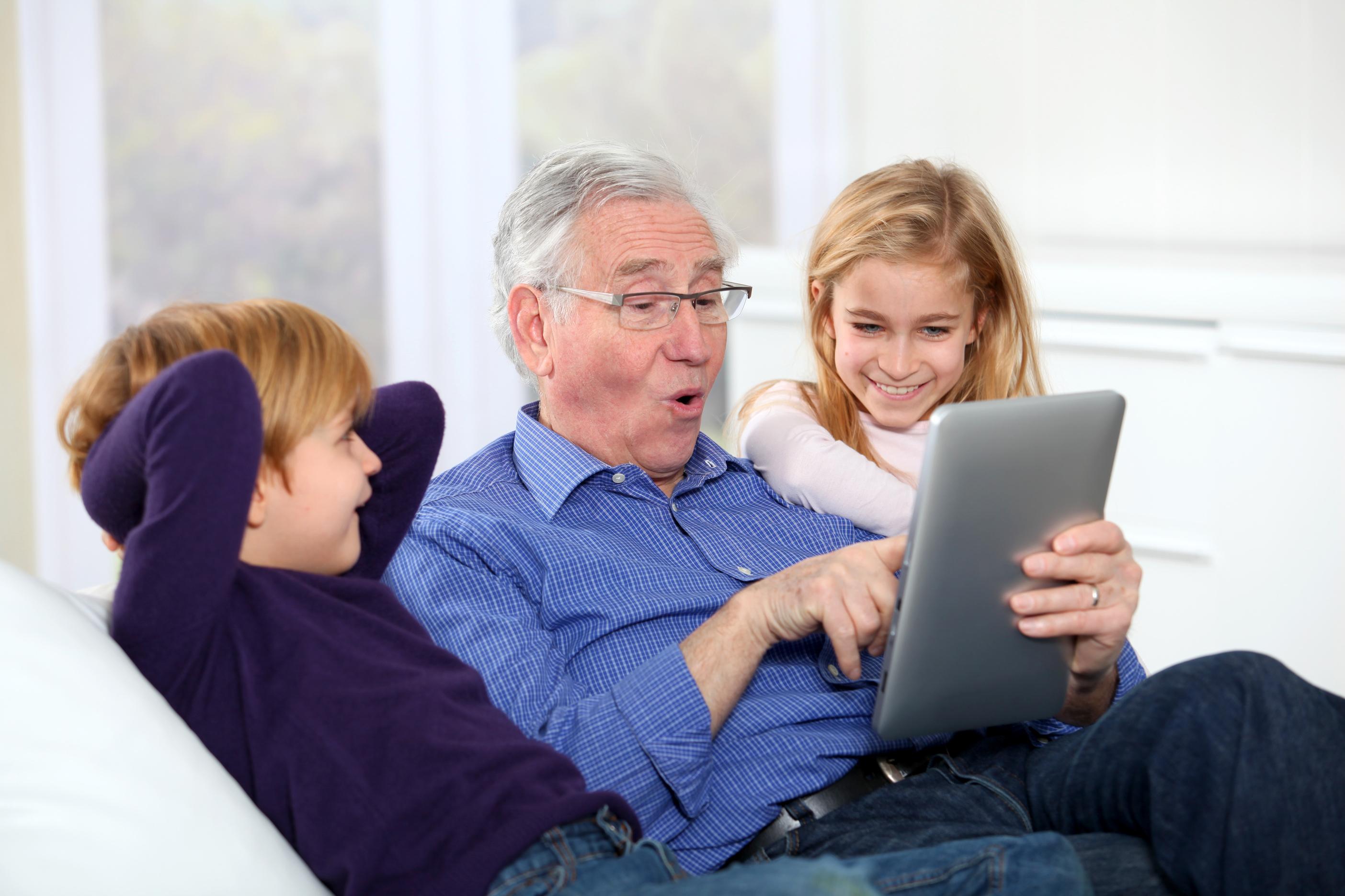 Grandfather sitting with grandchildren using a tablet
